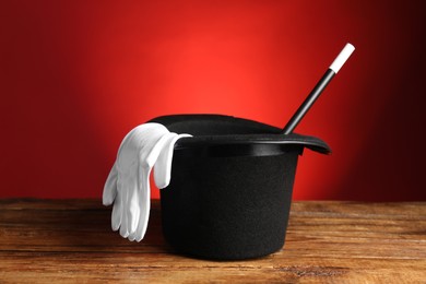 Photo of Magician's hat, gloves and wand on wooden table against red background