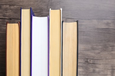 Photo of Collection of different books near wooden wall, closeup. Space for text