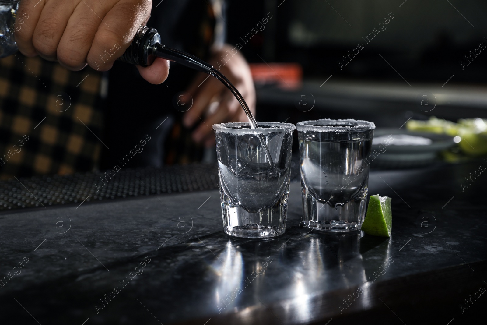 Photo of Bartender pouring Mexican Tequila into shot glasses at bar counter, closeup