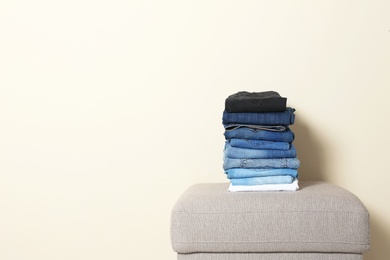 Photo of Stack of different jeans on ottoman against light background. Space for text