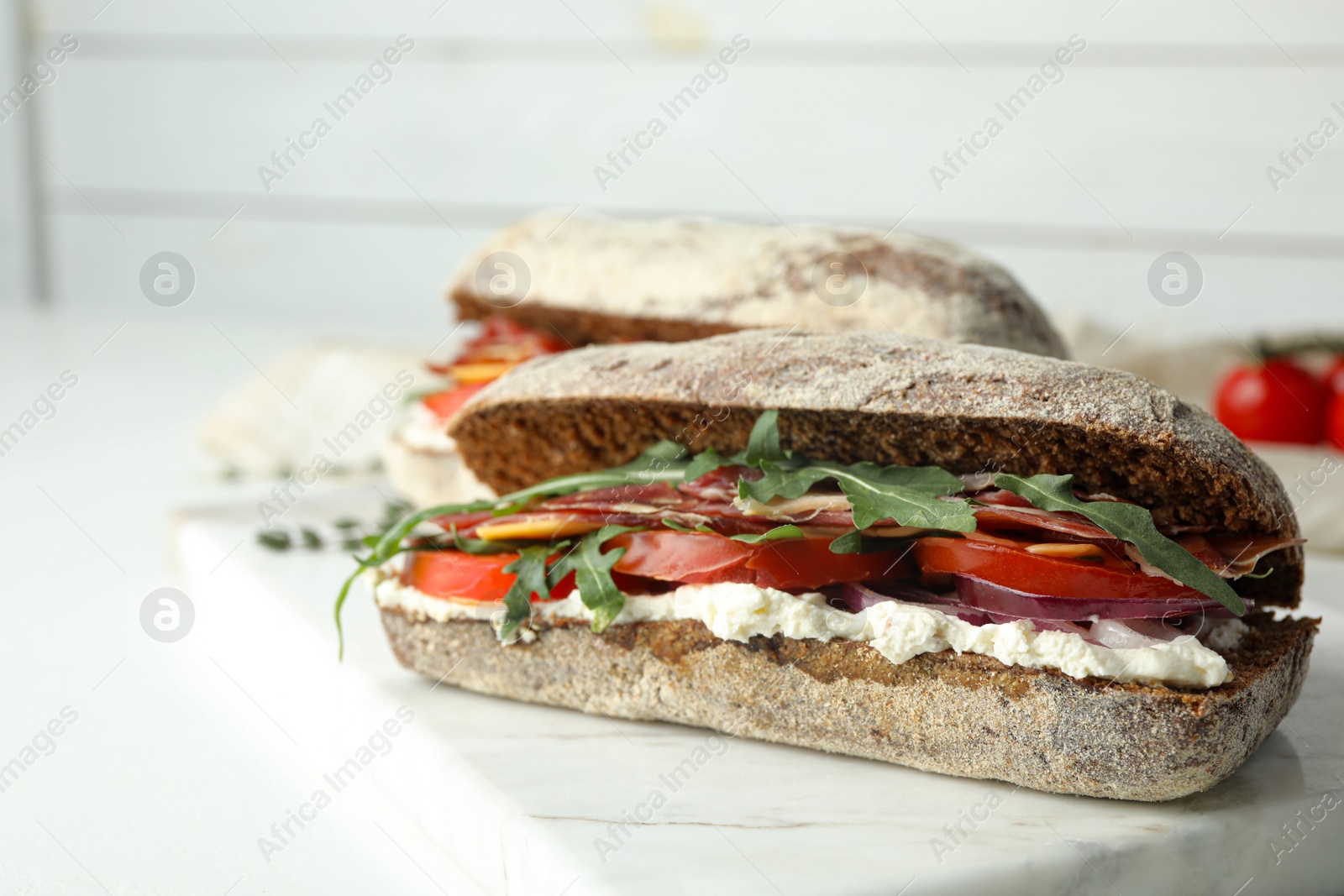 Photo of Delicious sandwiches with fresh vegetables and prosciutto on white table