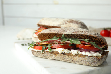 Delicious sandwiches with fresh vegetables and prosciutto on white table
