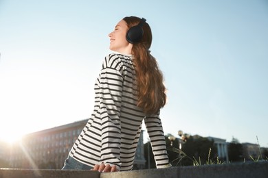 Photo of Smiling woman in headphones listening to music outdoors, low angle view