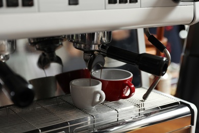 Photo of Aromatic coffee pouring into cups from modern machine, closeup