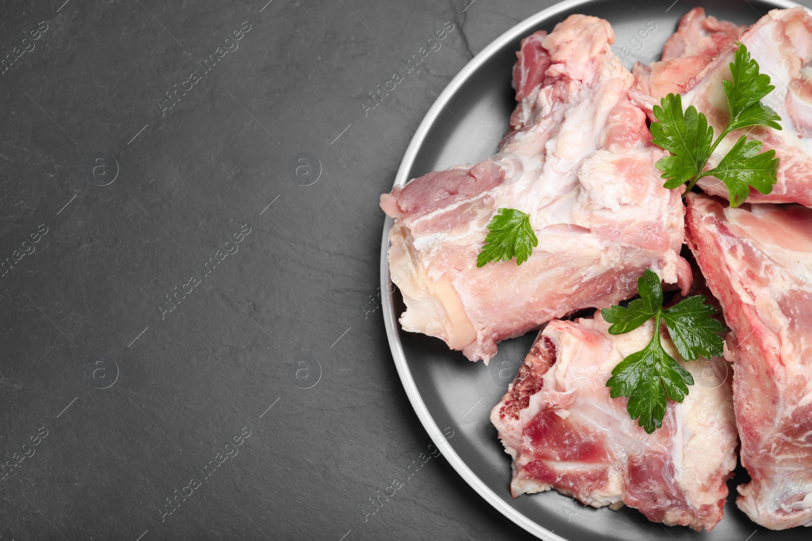 Photo of Plate with raw chopped meaty bones and parsley on black table, top view. Space for text