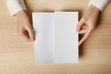 Woman holding blank brochure mock up on wooden table, top view