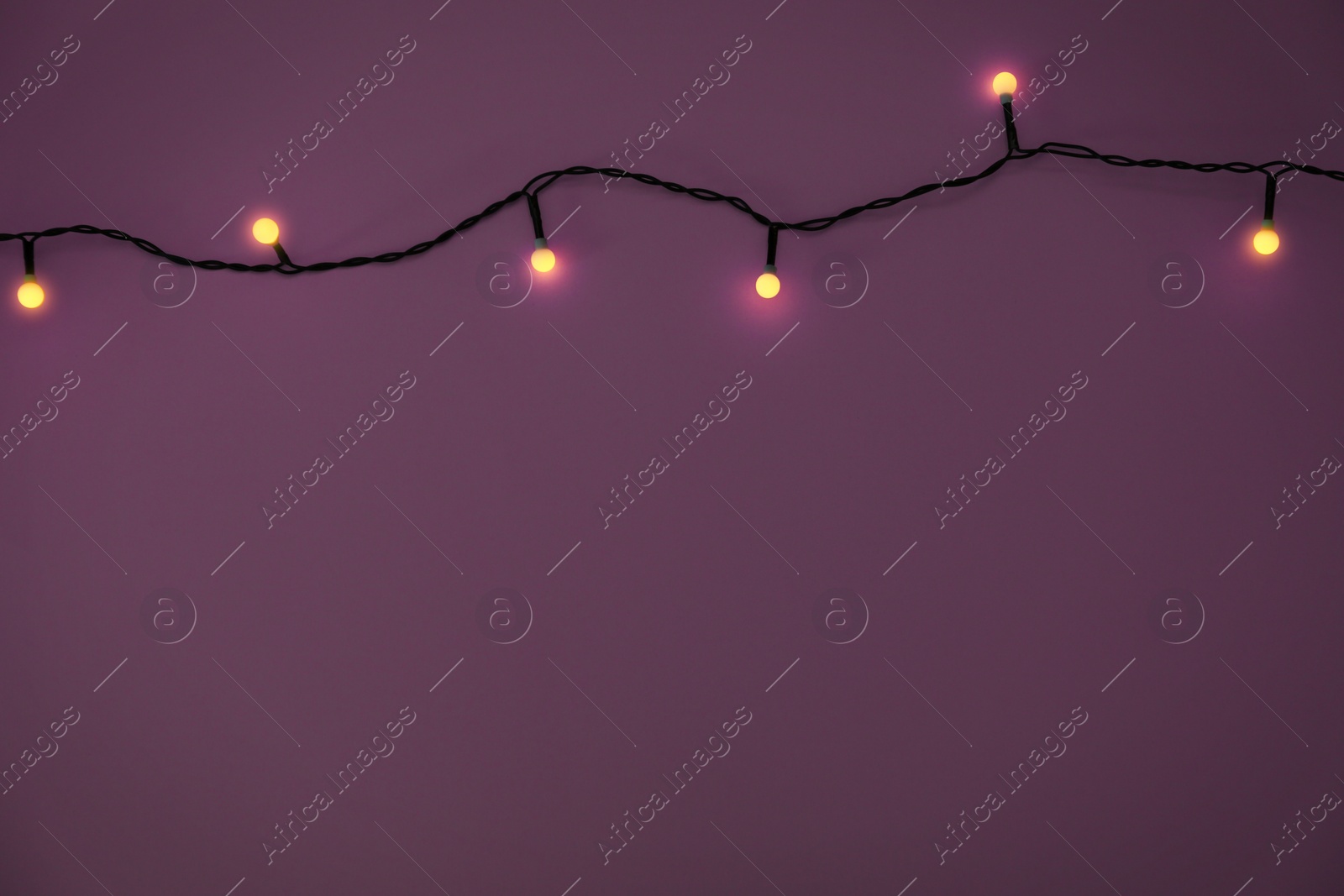 Photo of Glowing Christmas lights on violet background, top view. Space for text