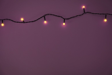 Photo of Glowing Christmas lights on violet background, top view. Space for text