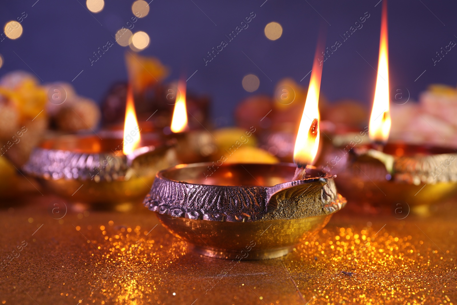 Photo of Diwali celebration. Diya lamps on shiny golden table against blurred lights, closeup