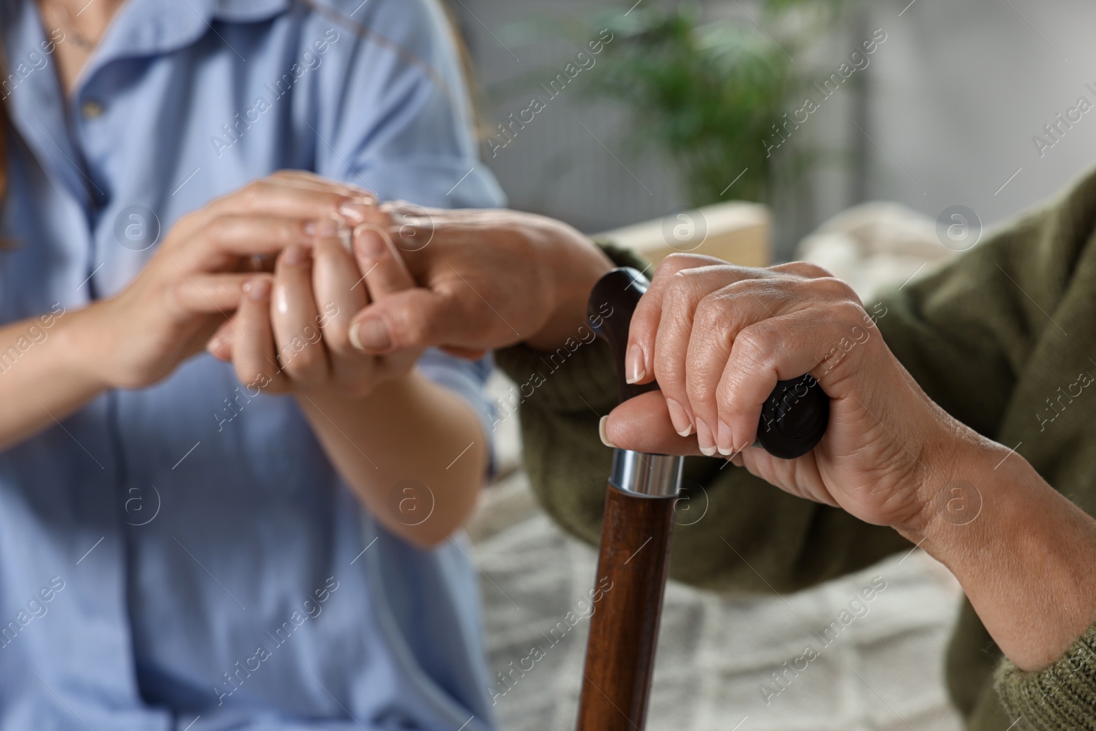 Photo of Caregiver and elderly woman with walking cane at home, closeup