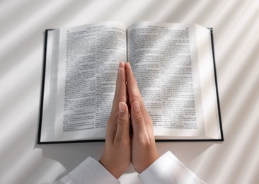 Above view of woman holding hands clasped while praying over Bible at white table