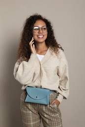 Photo of Beautiful African American woman with stylish waist bag on beige background