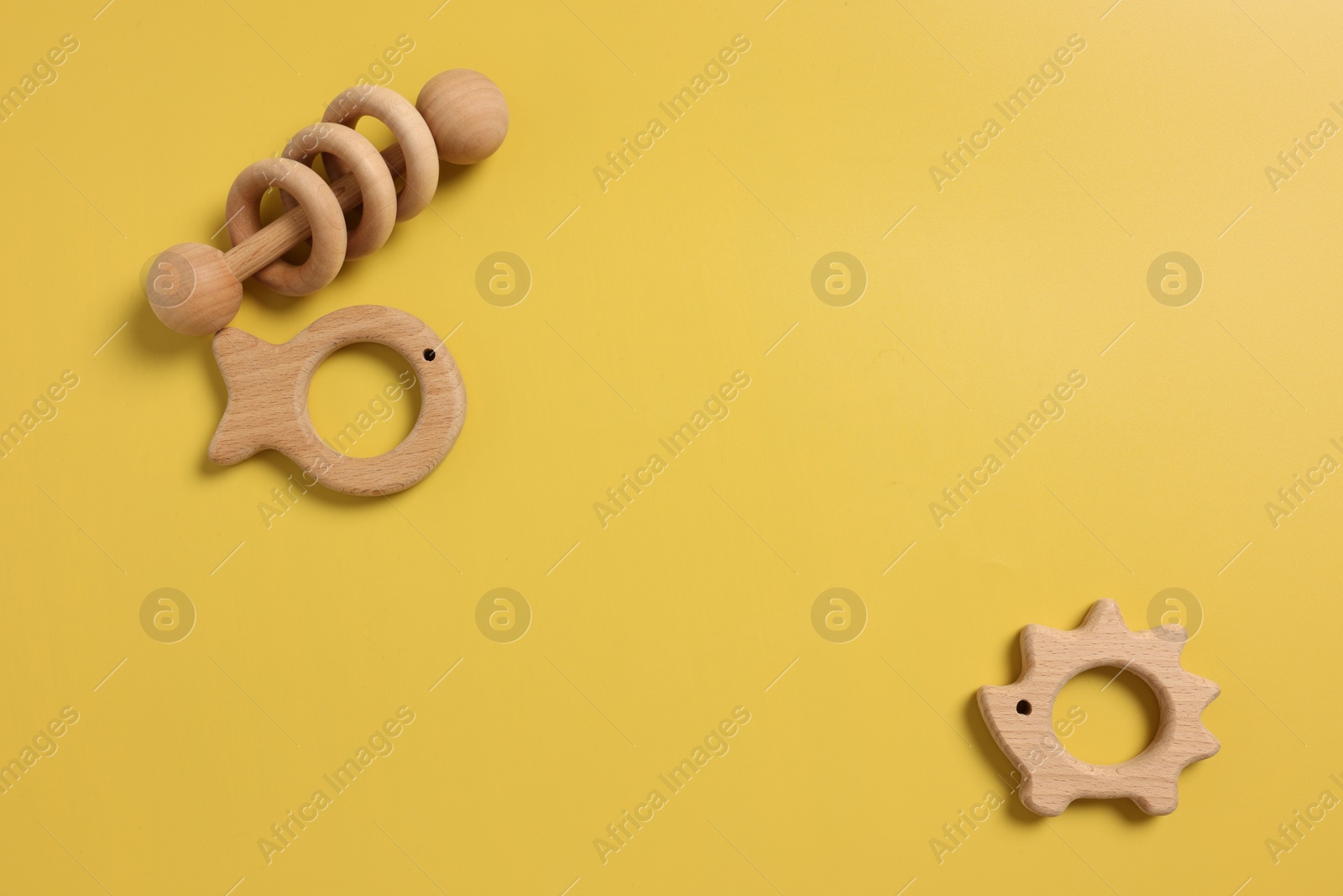 Photo of Baby accessories. Wooden rattle and teethers on yellow background, flat lay. Space for text