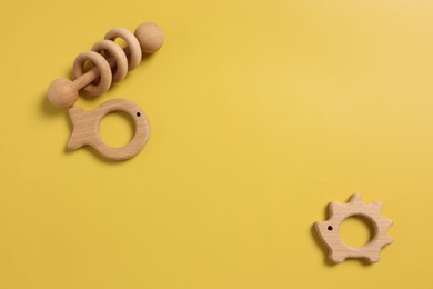 Photo of Baby accessories. Wooden rattle and teethers on yellow background, flat lay. Space for text