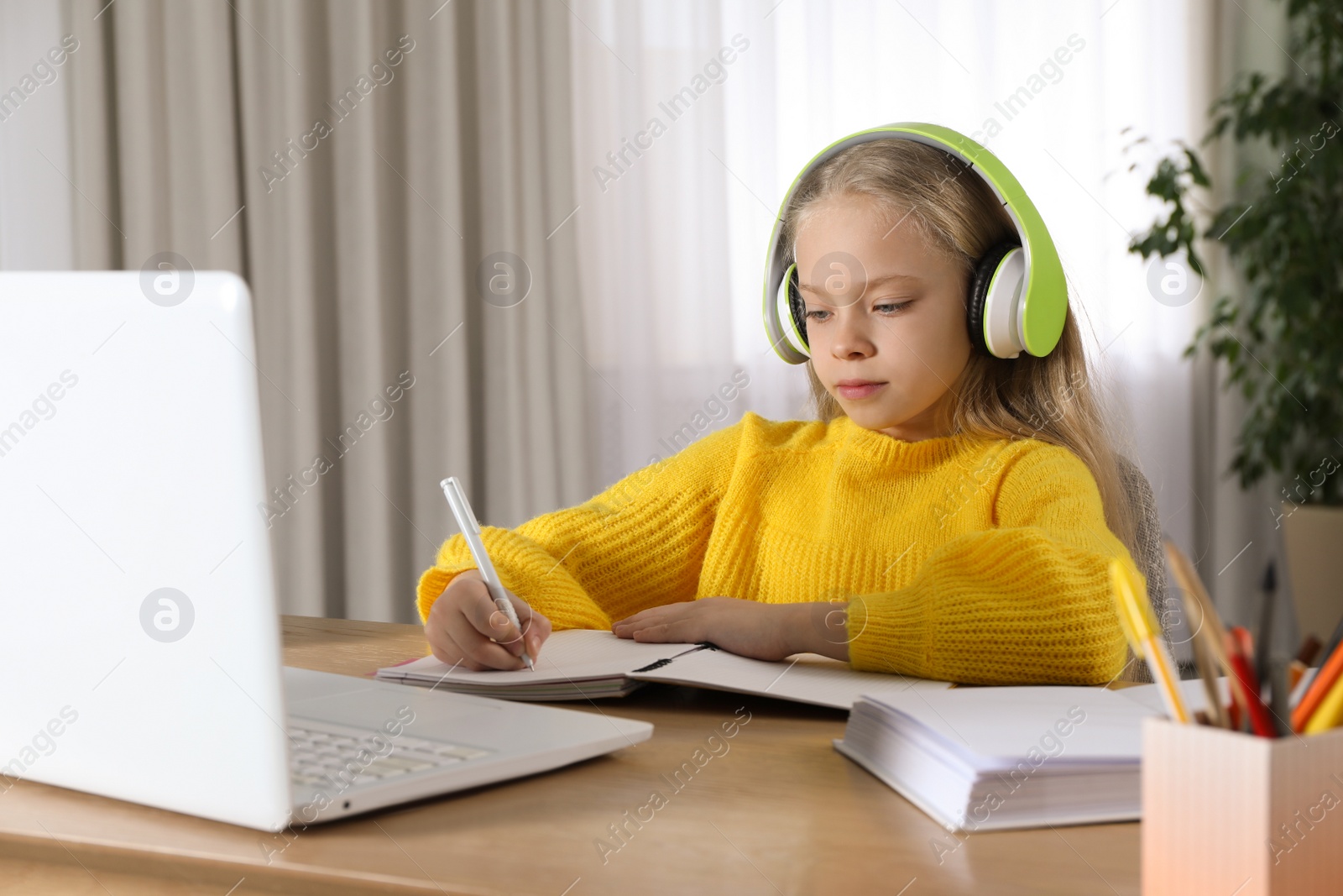 Photo of Cute little girl with modern laptop studying online at home. E-learning