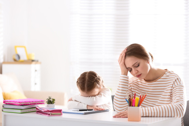 Photo of Upset mother and daughter doing homework together at table indoors