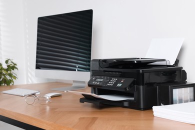 Modern printer with paper near computer on wooden table in office