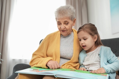 Photo of Cute girl and her grandmother reading book at home