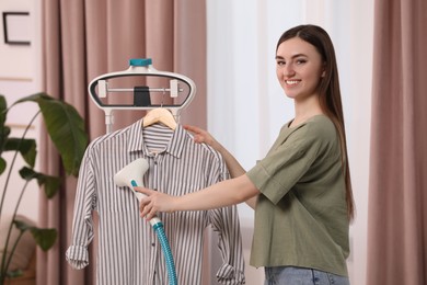 Photo of Woman steaming shirt on hanger at home