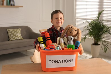 Photo of Cute little boy holding donation box with toys at home