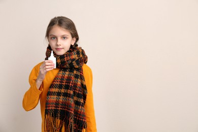 Photo of Sick little girl with nasal spray on beige background. Space for text