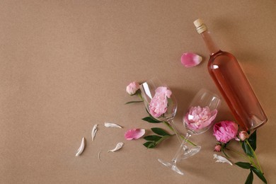 Bottle of rose wine, glasses and beautiful pink peonies on brown background, flat lay. Space for text