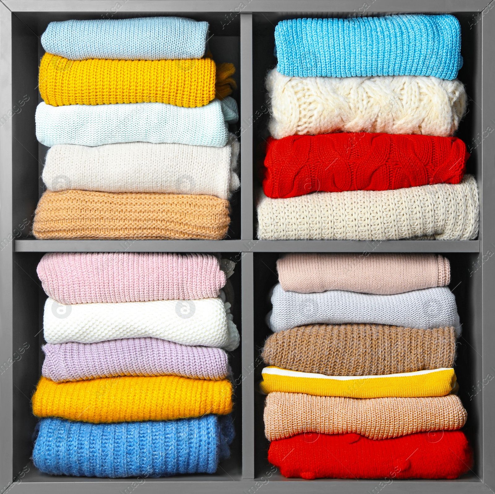 Photo of Many knitted winter clothes stacked on shelves near white background