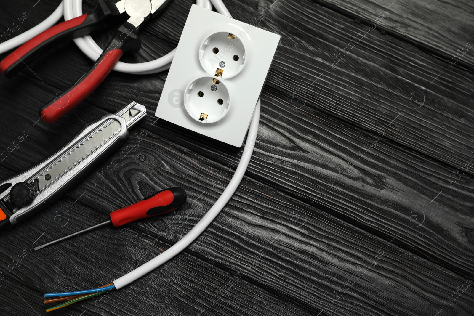 Photo of Set of electrician's tools and power socket on black wooden table, flat lay. Space for text