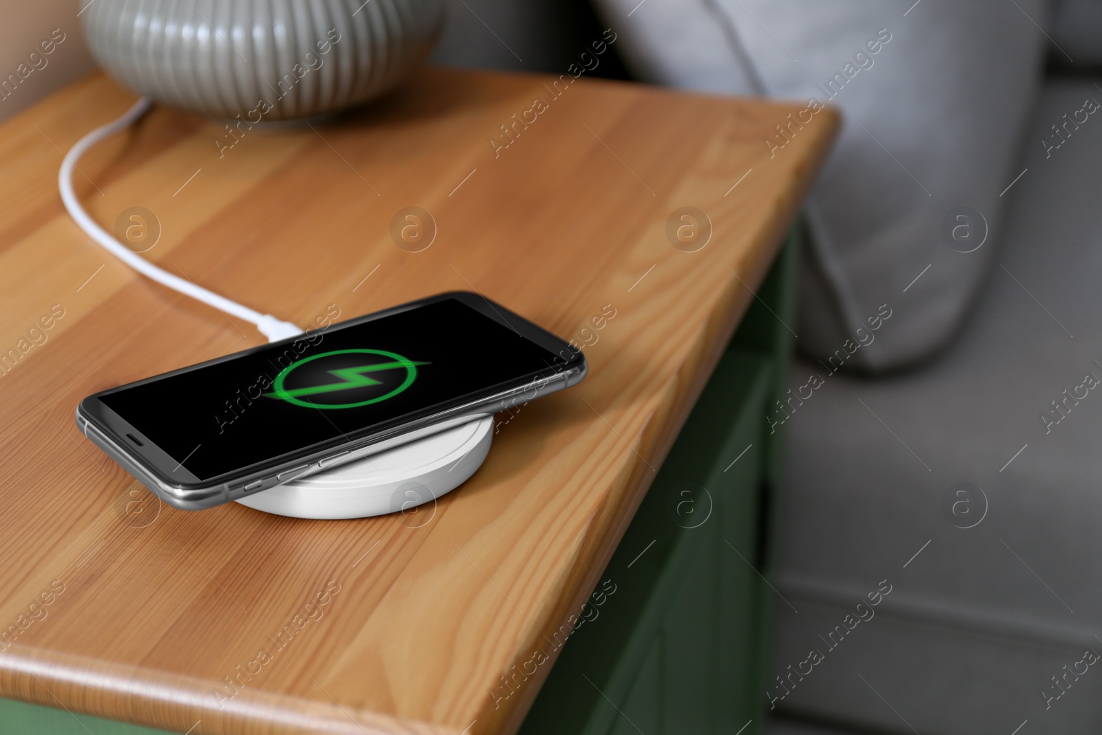 Photo of Smartphone charging on wireless pad in room. Space for text