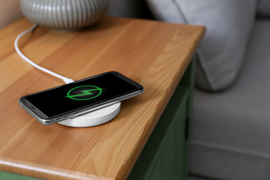 Photo of Smartphone charging on wireless pad in room. Space for text