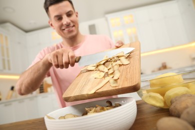 Photo of Man with cutting board and knife scraping vegetable peels into bowl in kitchen