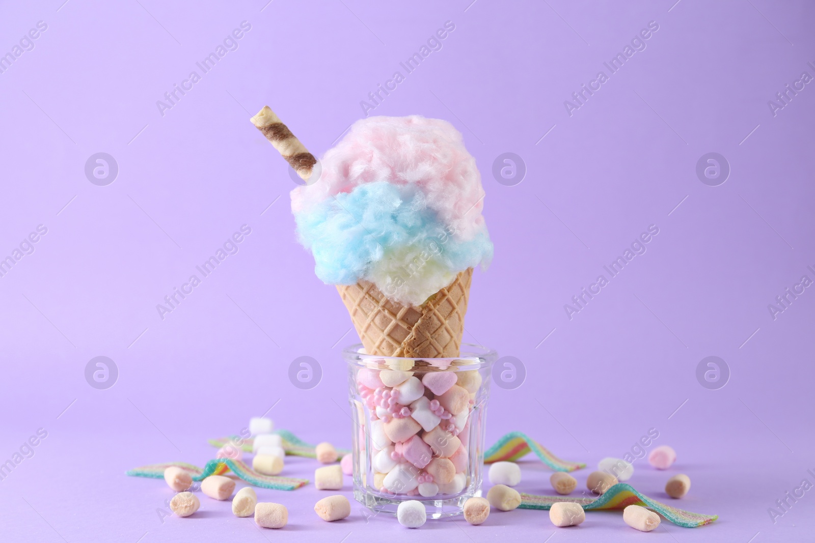 Photo of Sweet cotton candy in waffle cone and marshmallows on purple background