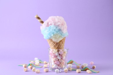 Photo of Sweet cotton candy in waffle cone and marshmallows on purple background