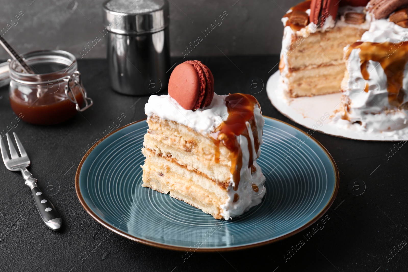 Photo of Piece of delicious homemade cake with caramel sauce and macaron on table