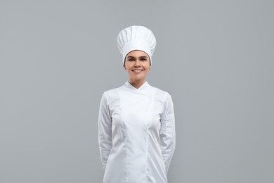 Photo of Happy female chef wearing uniform and cap on light grey background