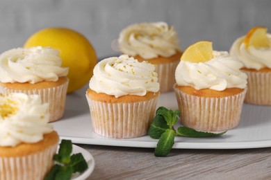 Photo of Delicious lemon cupcakes with white cream and mint on table, closeup