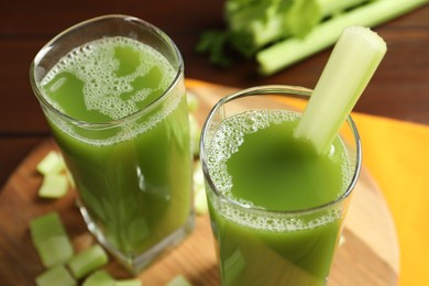 Glasses of delicious celery juice and vegetables on wooden board, closeup