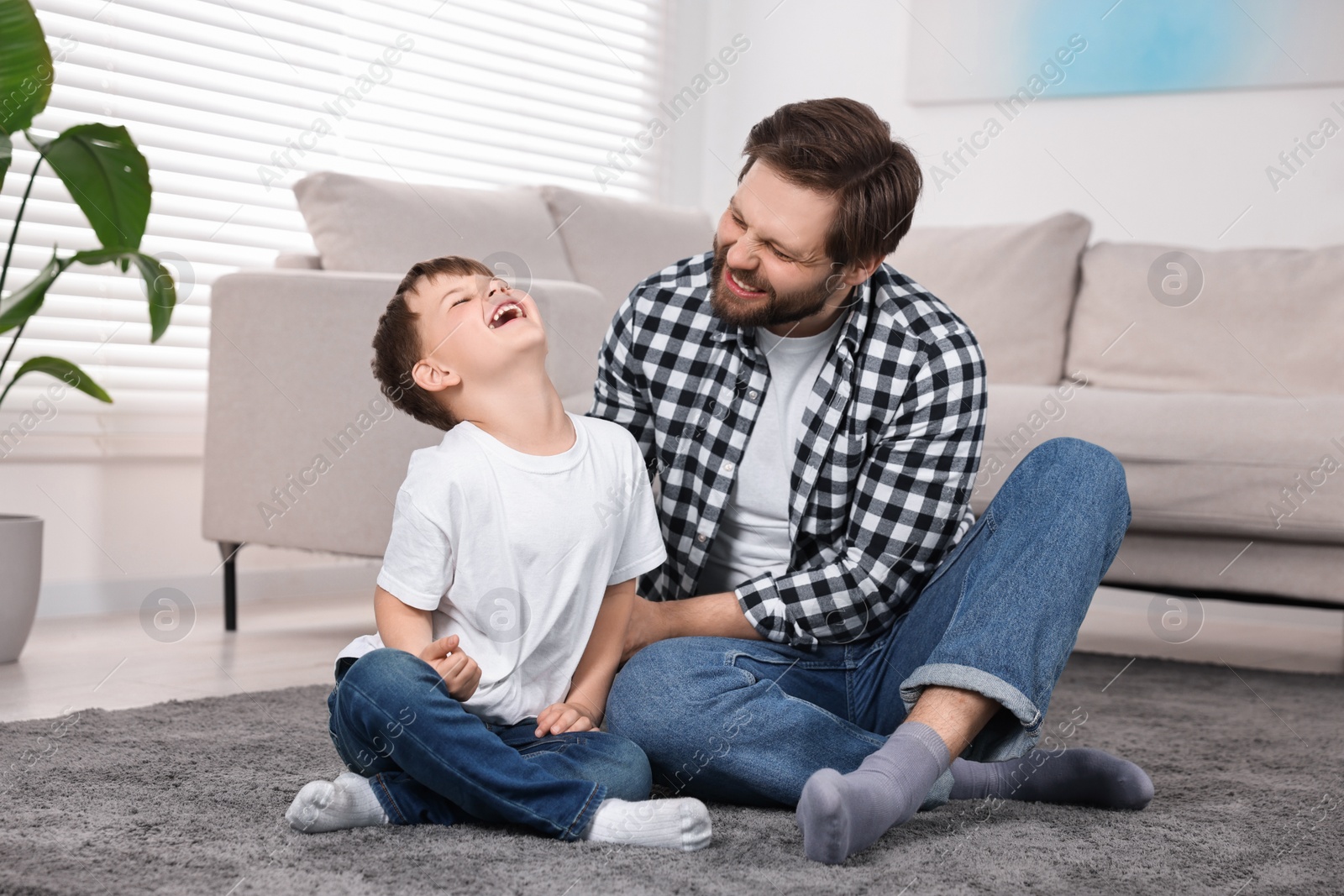 Photo of Happy dad and son having fun on carpet at home