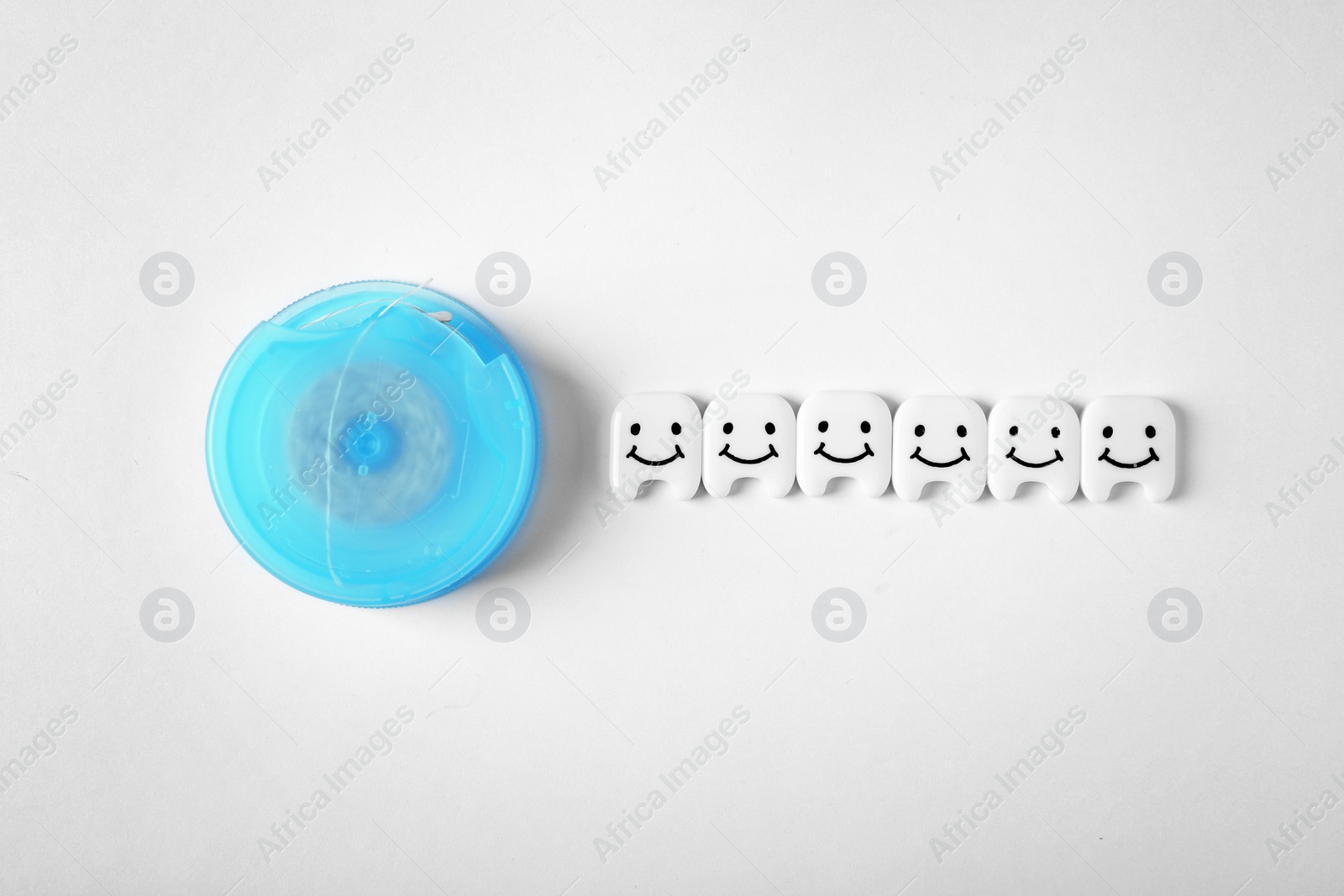 Photo of Small plastic teeth with cute faces and dental floss on white background, top view