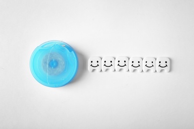 Photo of Small plastic teeth with cute faces and dental floss on white background, top view
