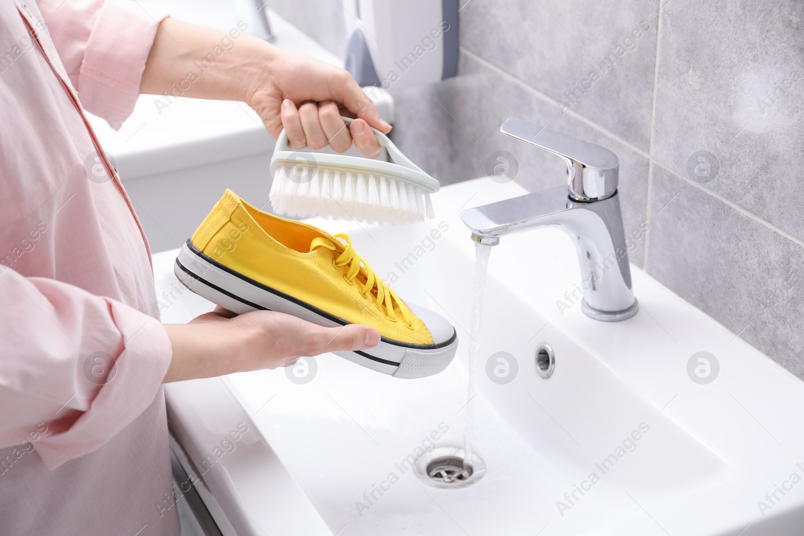 Photo of Woman washing stylish sneakers with brush in sink, closeup