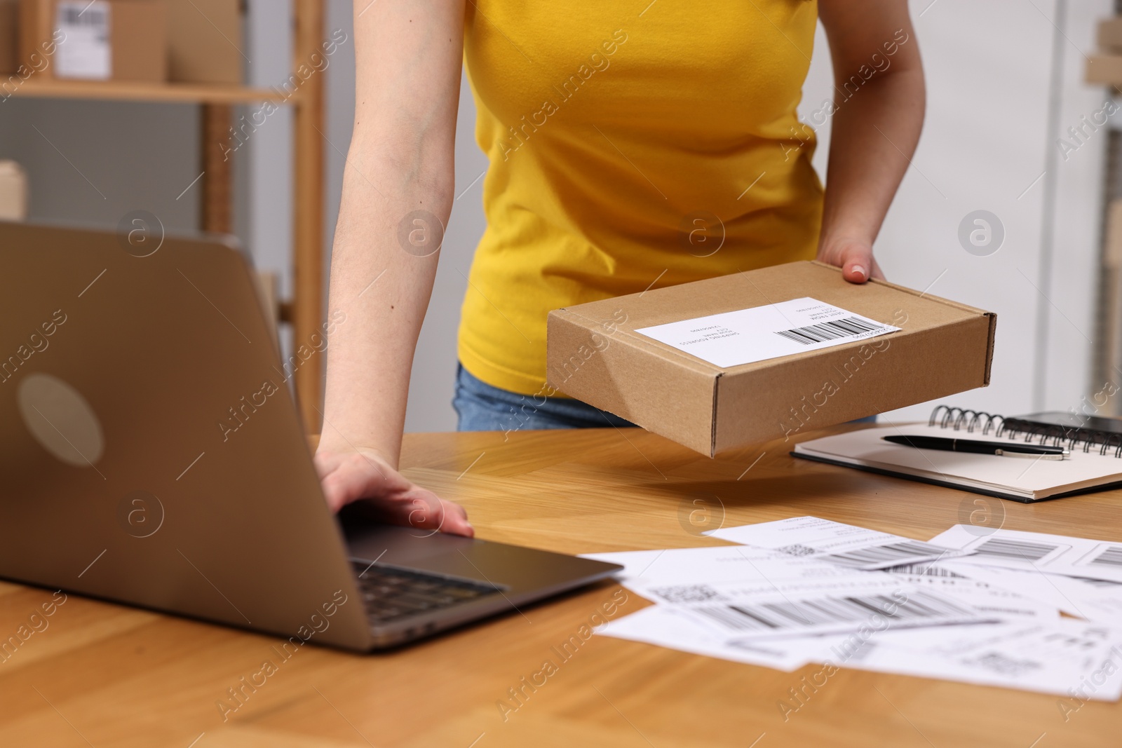 Photo of Parcel packing. Post office worker with box using laptop at wooden table indoors, closeup