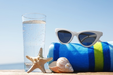 Photo of Wooden deck with glass of refreshing drink and beach accessories on hot summer day