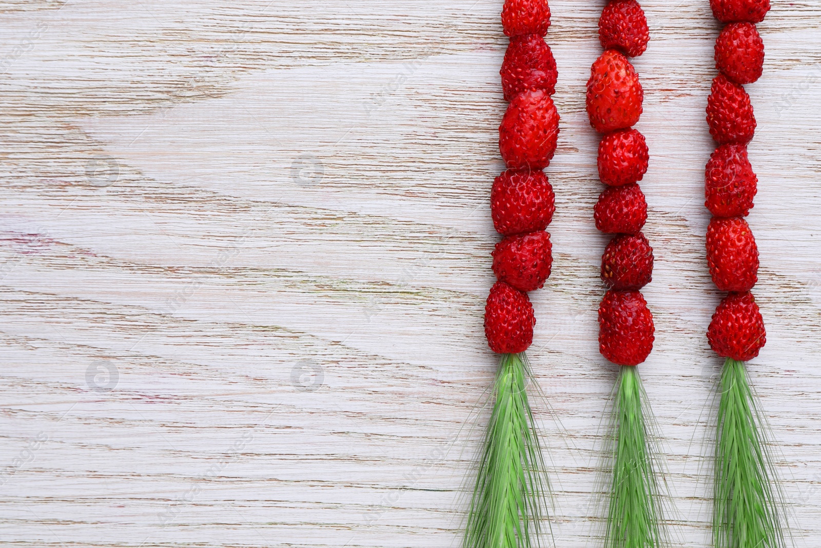 Photo of Grass stems with wild strawberries on white wooden table, flat lay. Space for text