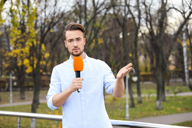 Photo of Young male journalist with microphone working in park