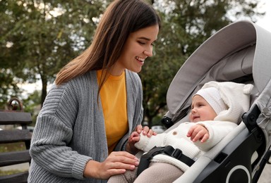 Happy mother with her adorable baby in stroller sitting on bench outdoors