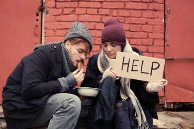 Photo of Poor young couple with HELP sign and bread on dirty street