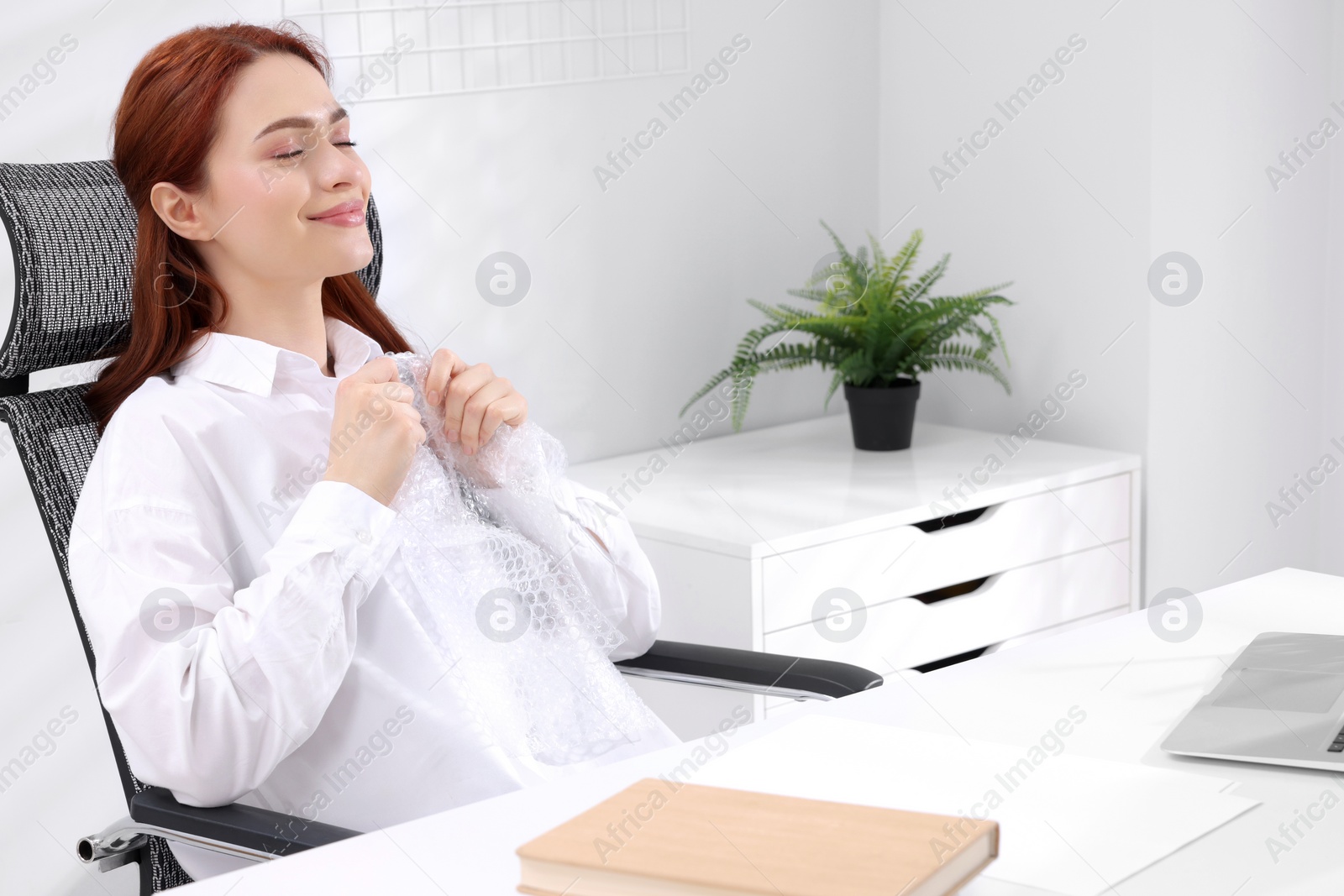 Photo of Woman popping bubble wrap at desk in office. Stress relief