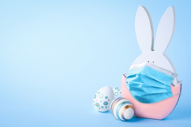 Image of COVID-19 pandemic.COVID-19 pandemic. Easter bunny figure in protective mask on light blue background, space for text