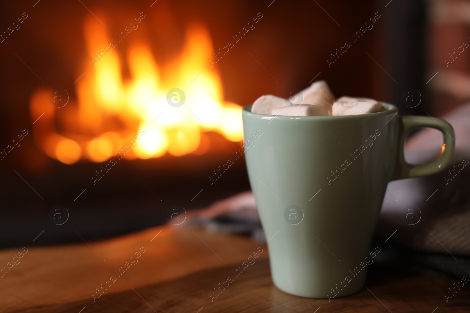 Photo of Delicious sweet cocoa with marshmallows and blurred fireplace on background